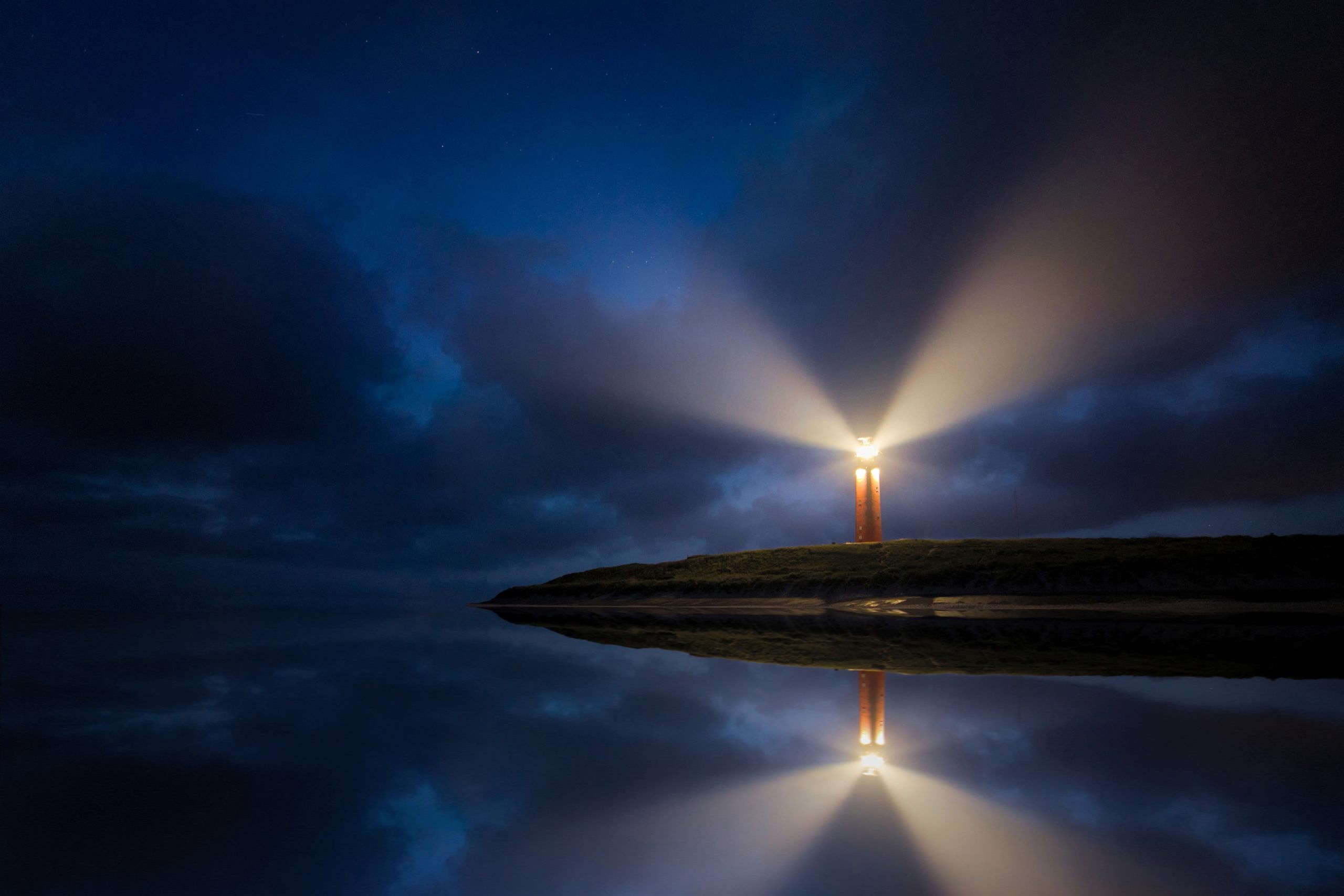 Leuchtturm bei Nacht mit Reflexion im Wasser